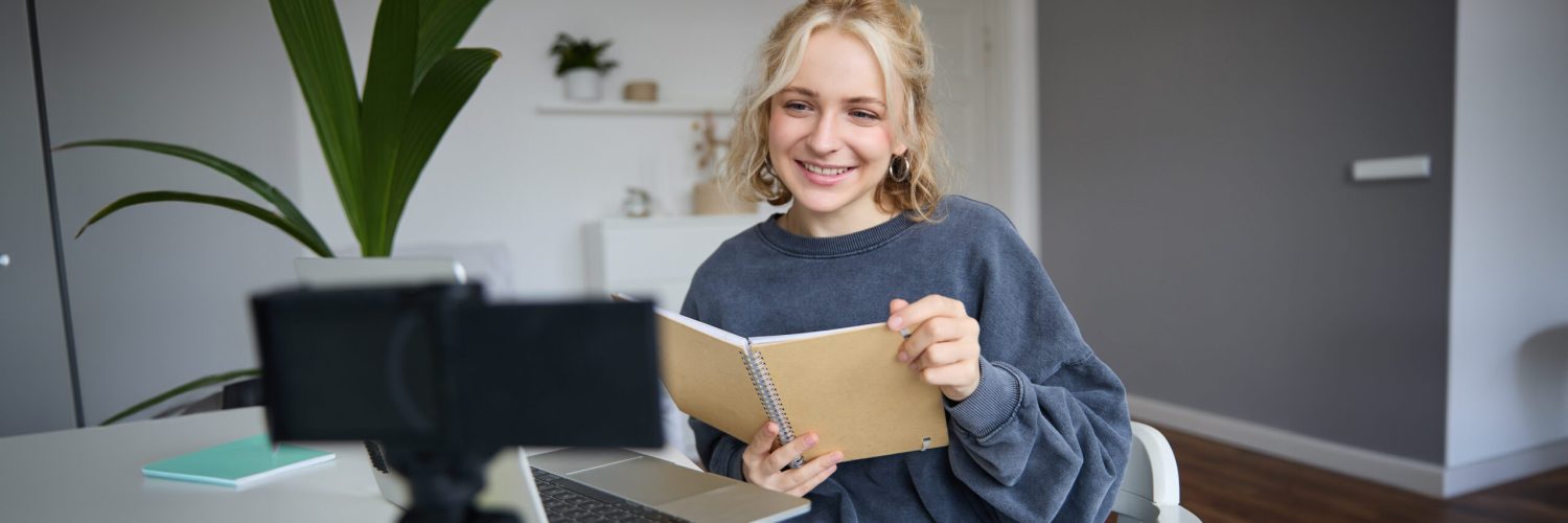 Portrait of young woman using digital camera and laptop, studying, connect to online live stream, records video for vlog, creating content, holding notebook, sitting in room.
